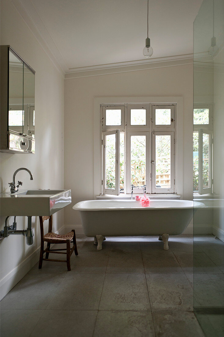 Weißes Badezimmer im schlichten Landhausstil mit freistehender Badewanne und Steinfliesenboden
