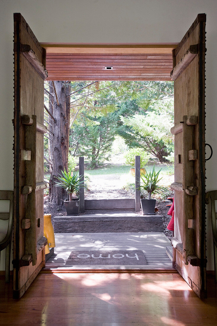 Blick durch geöffnete rustikale Holzflügeltüren auf sommerlichen Garten