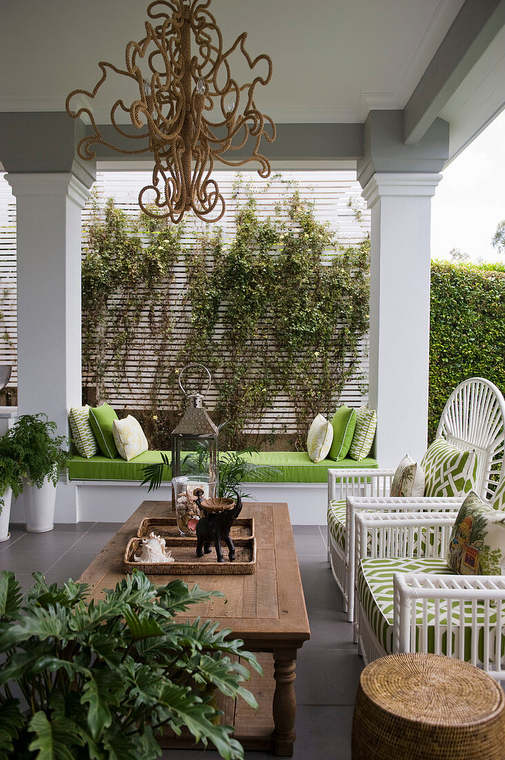 Holztisch mit weißen Pfauenstühlen auf überdachter Terrasse mit dekorativen Säulen
