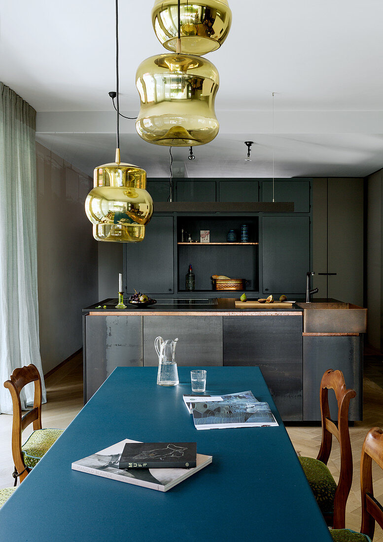Metall-Esstisch mit blauer Platte vor moderner Küche in Grautönen