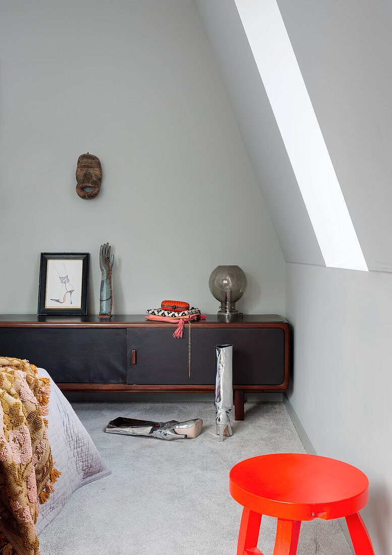 Orange stool and low sideboard in bedroom with slightly sloping wall