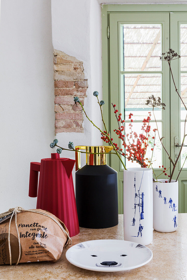 Zweige in modernen Vasen und Thermoskannen in rustikaler Küche