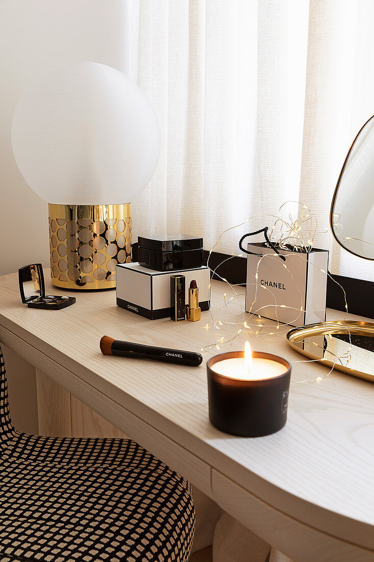 Lit candle, make-up and spherical lamp on console table