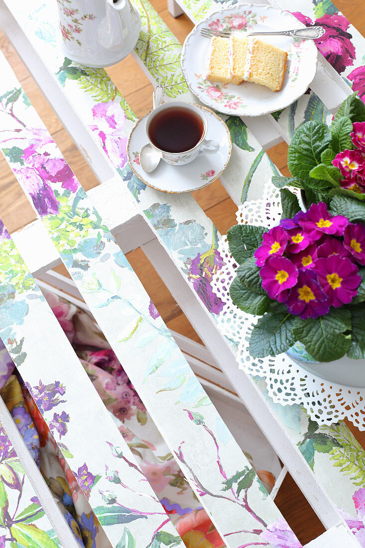 Primulas, tea and cake on DIY palette table decorated with springlike floral pattern