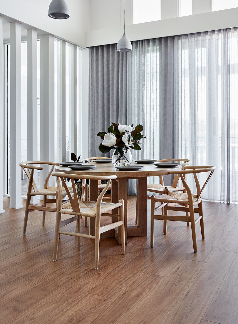 Designerstühle am runden Holztisch vor Fensterfronten mit Gardinen