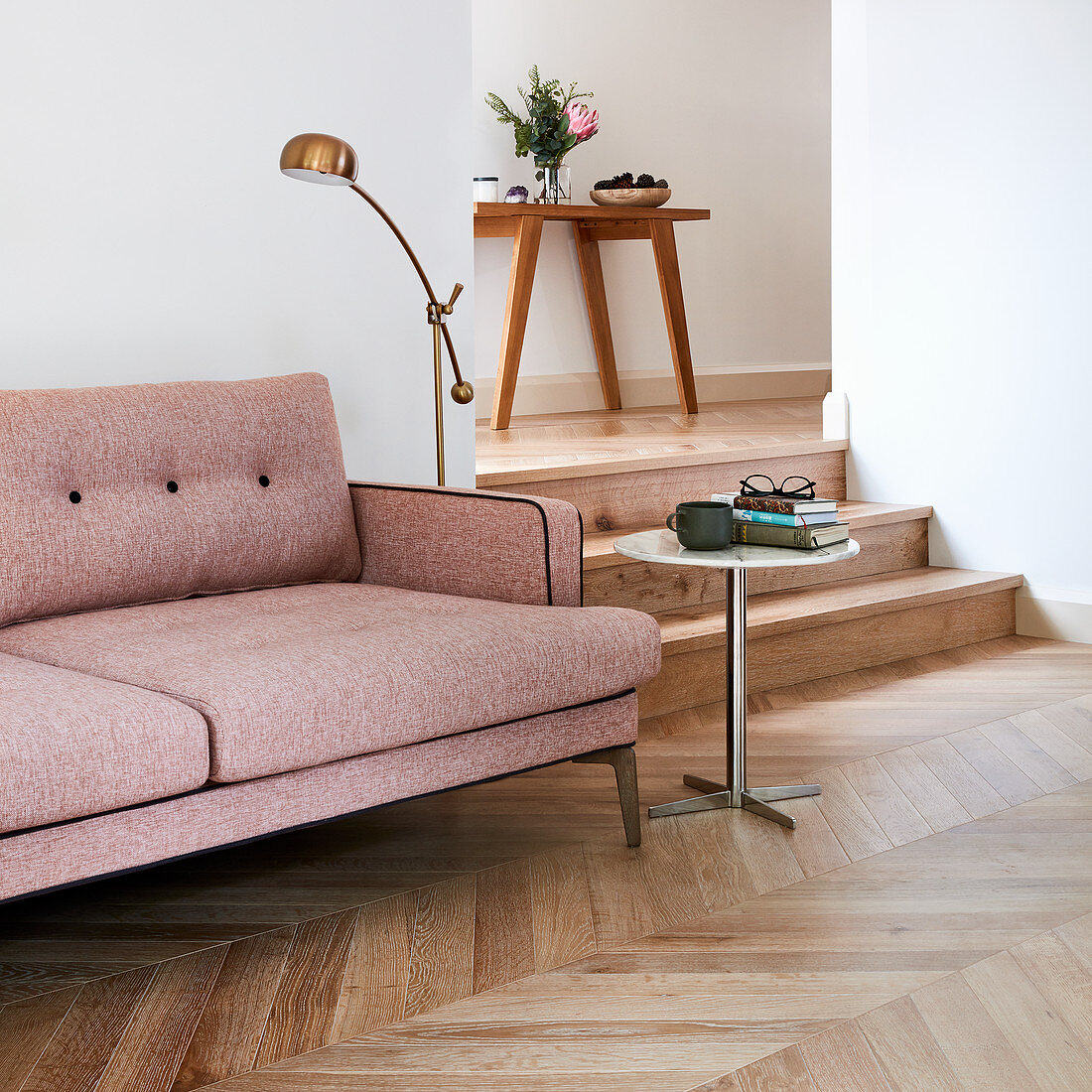 Dusky pink sofa on herringbone parquet floor next to steps leading to hallway