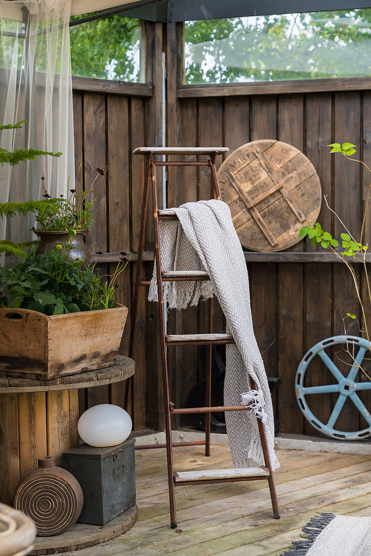 Plaid an einer Holzleiter auf der Terrasse mit Vintage-Deko