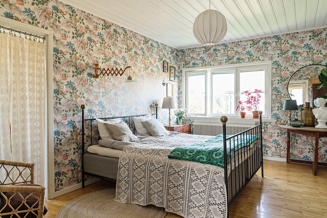 Metal bed in vintage-style bedroom with floral wallpaper