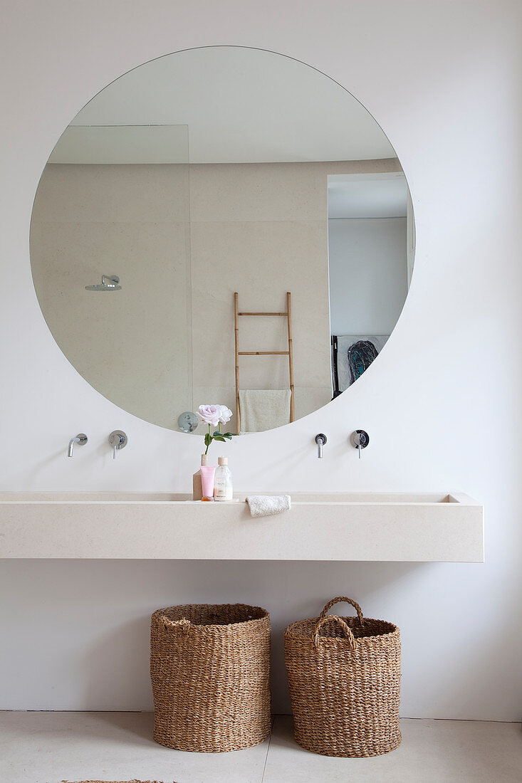 Large round mirror above sink with two baskets below