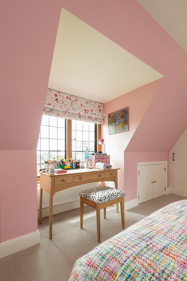 Desk below window in attic bedroom with pink walls