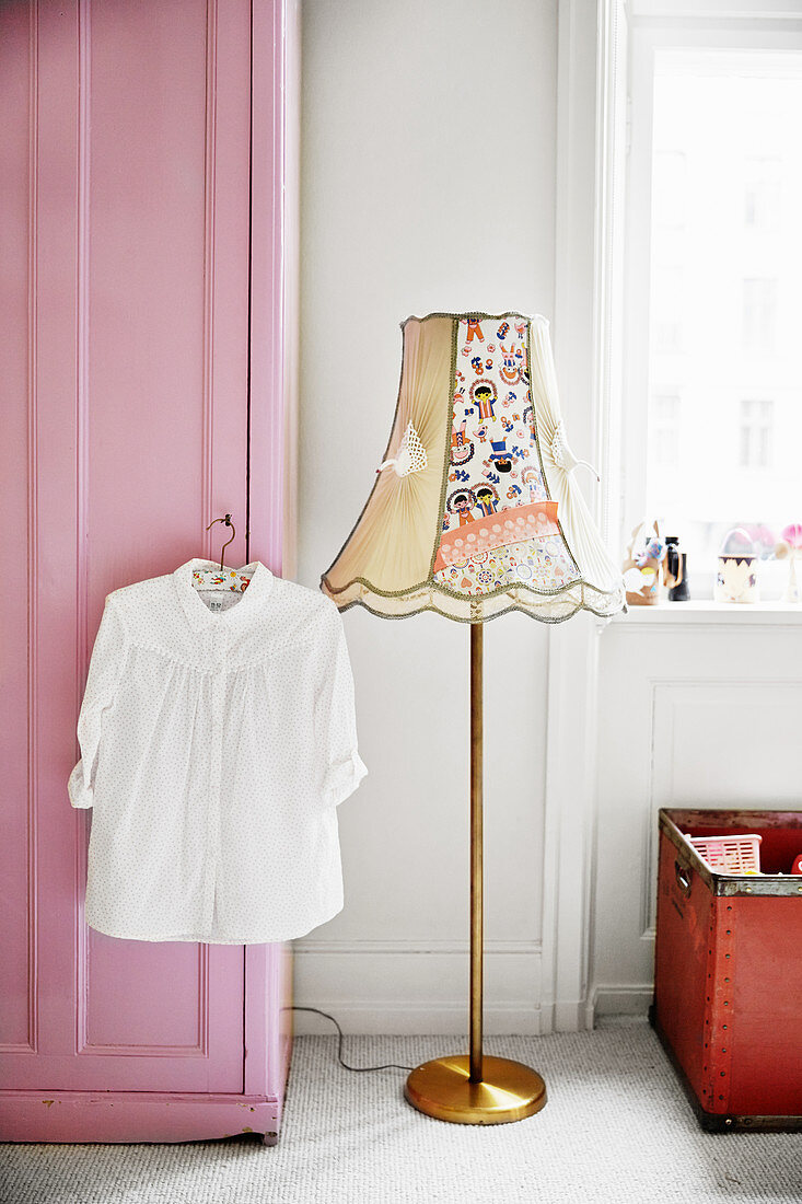 White blouse hung on pink wardrobe and standard lamp in child's bedroom