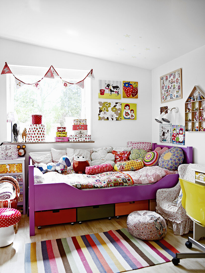 Scatter cushions and quilt on child's bed, bunting above window and decorations on walls in girl's bedroom