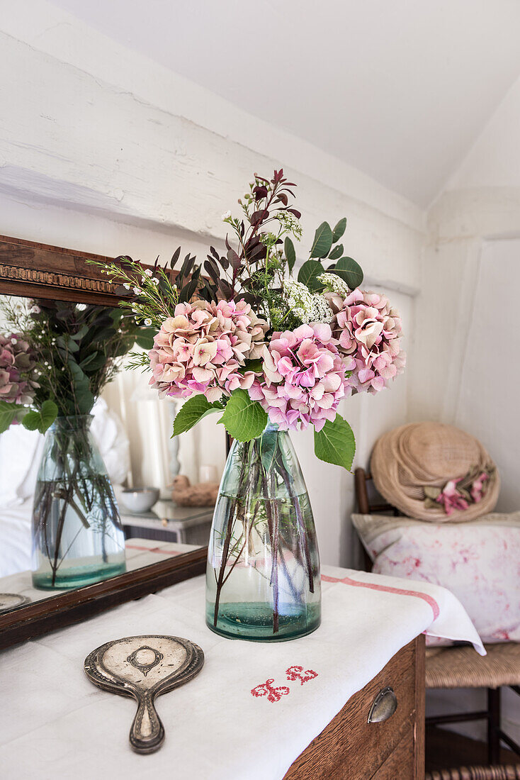 Vase mit rosa Hortensien, Handspiegel und antiker Spiegel auf Kommode