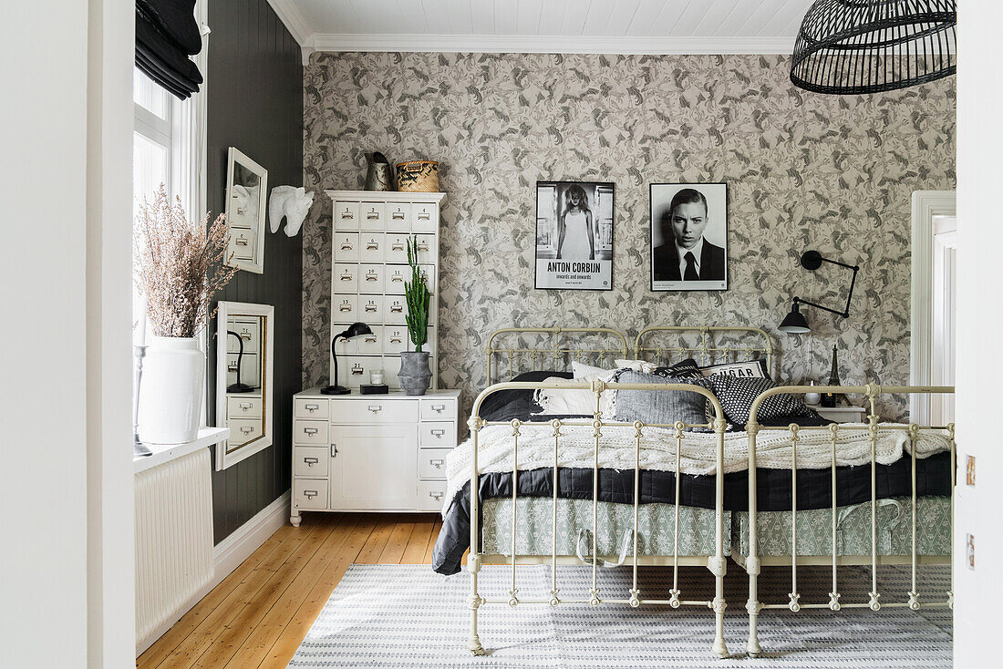 Old metal twin beds below black-and-white photographs on wallpapered wall