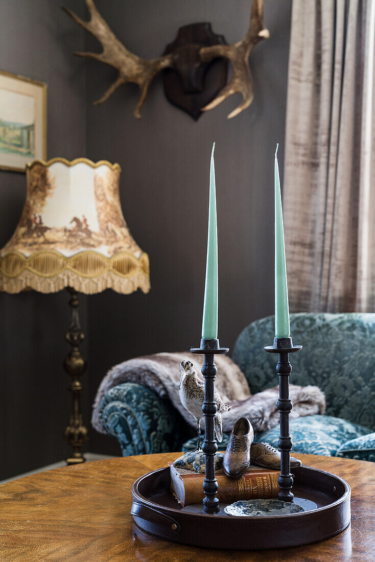 Tray with candles on antique coffee table, floor lamp and antlers in the background