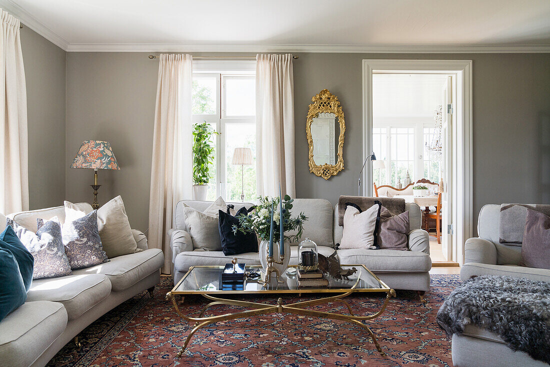 Upholstered suite around antique glass table and gilt-framed mirror in living room with grey walls