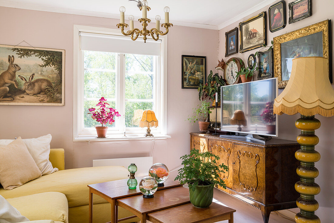 Antiker Schrank mit Fernseher, darüber Bildersammung im Wohnzimmer mit rosa Wänden