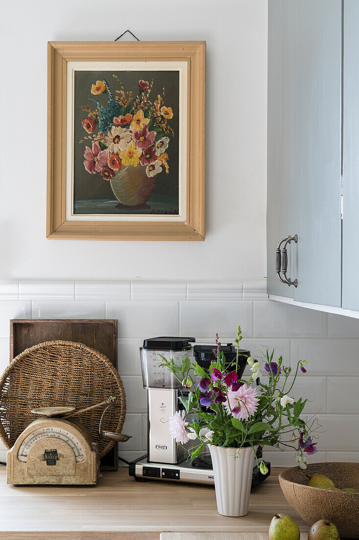 Bouquet of flowers, mixer and vintage scales on kitchen worksurface below floral artwork on wall