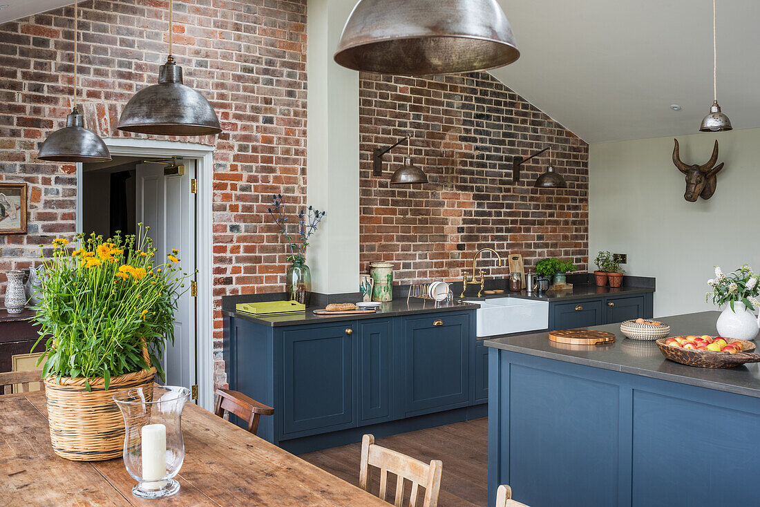 Modern country kitchen with blue cabinets, brick wall and industrial lamps