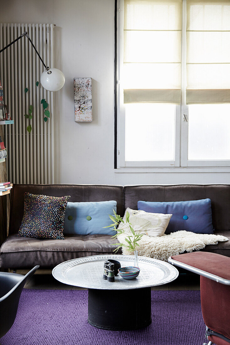 Couchtisch und graues Sofa mit Kissen vor Fenster im Wohnzimmer