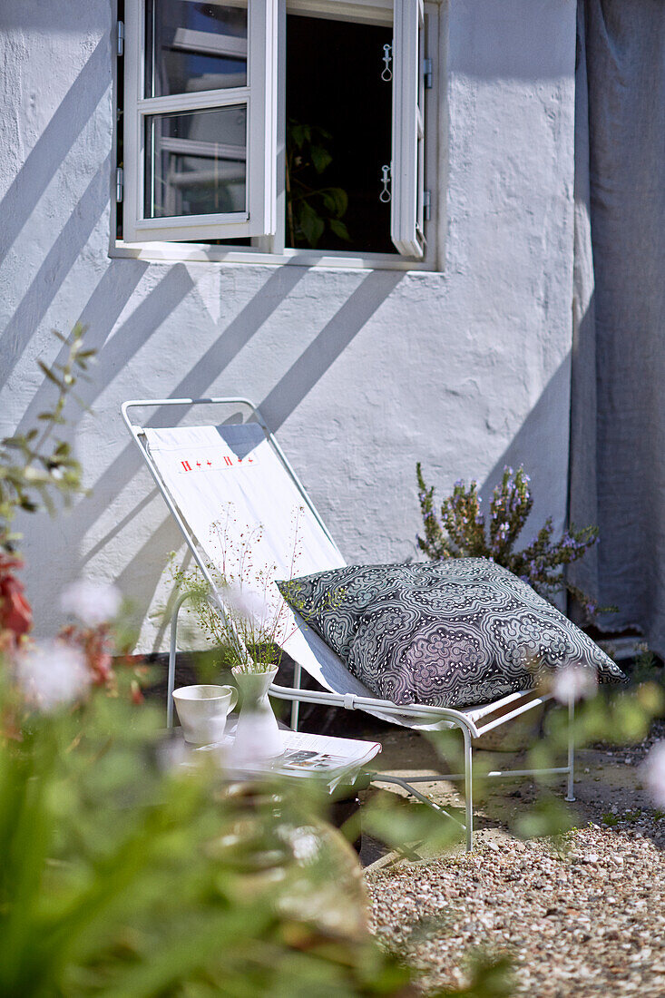 Deckchair with cushions under window on gravel terrace