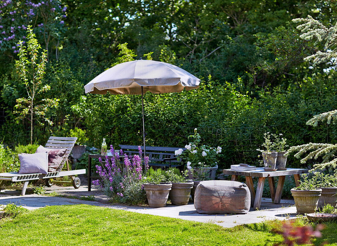 Terrassenplatz mit Outdoormöbeln, Blumen und Sonneschirm in sommerlichem Garten
