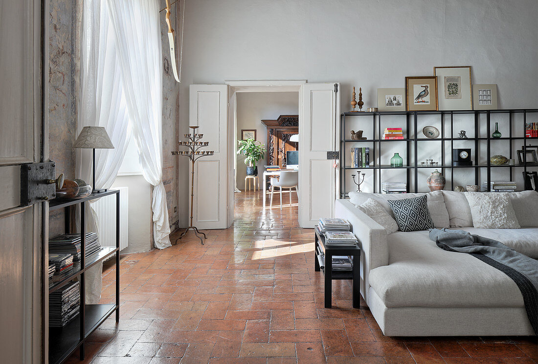 Offene Regale und helles Sofa in hohem Wohnzimmer mit Terrakottafliesen
