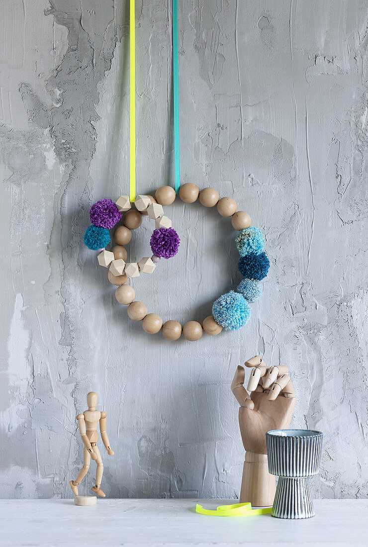 Wreaths of wooden beads and pompoms hung on wall with grey, structured, plaster surface