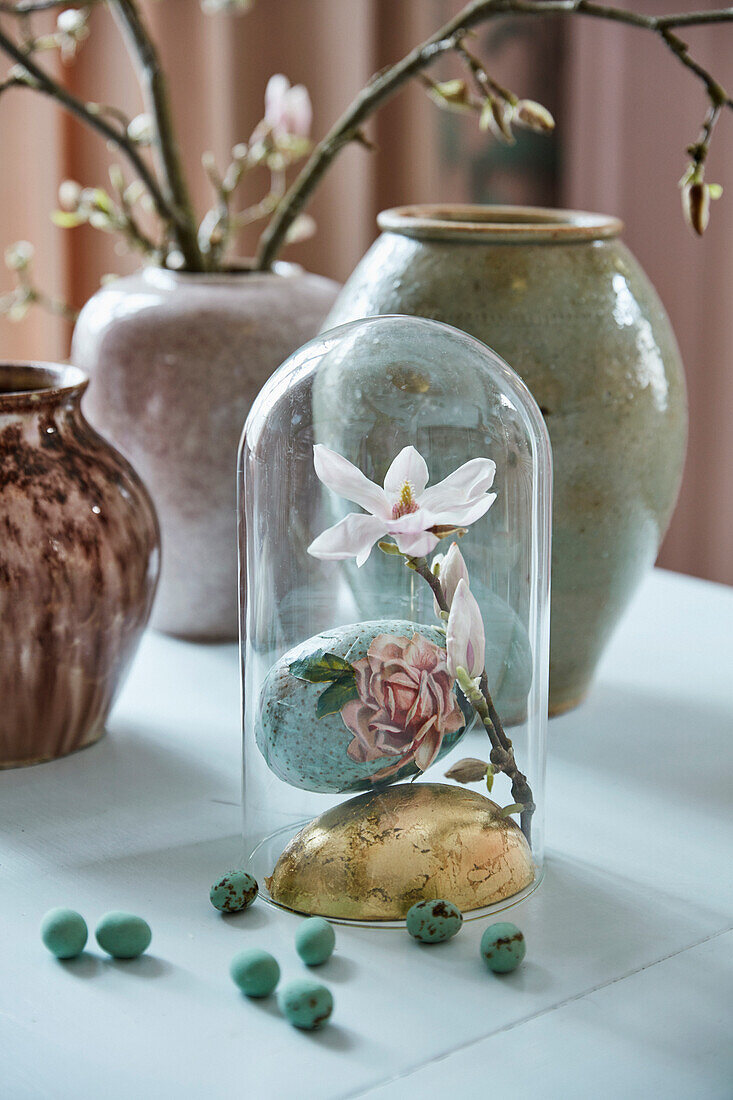 Ostereier und Magnolienblüte unter Glashaube