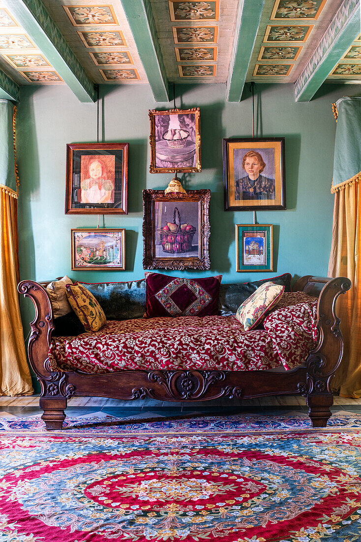 Antique sofa below gallery of paintings on green wall