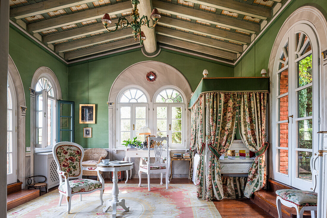 Bed behind curtains in green-painted room with antique tables and chairs