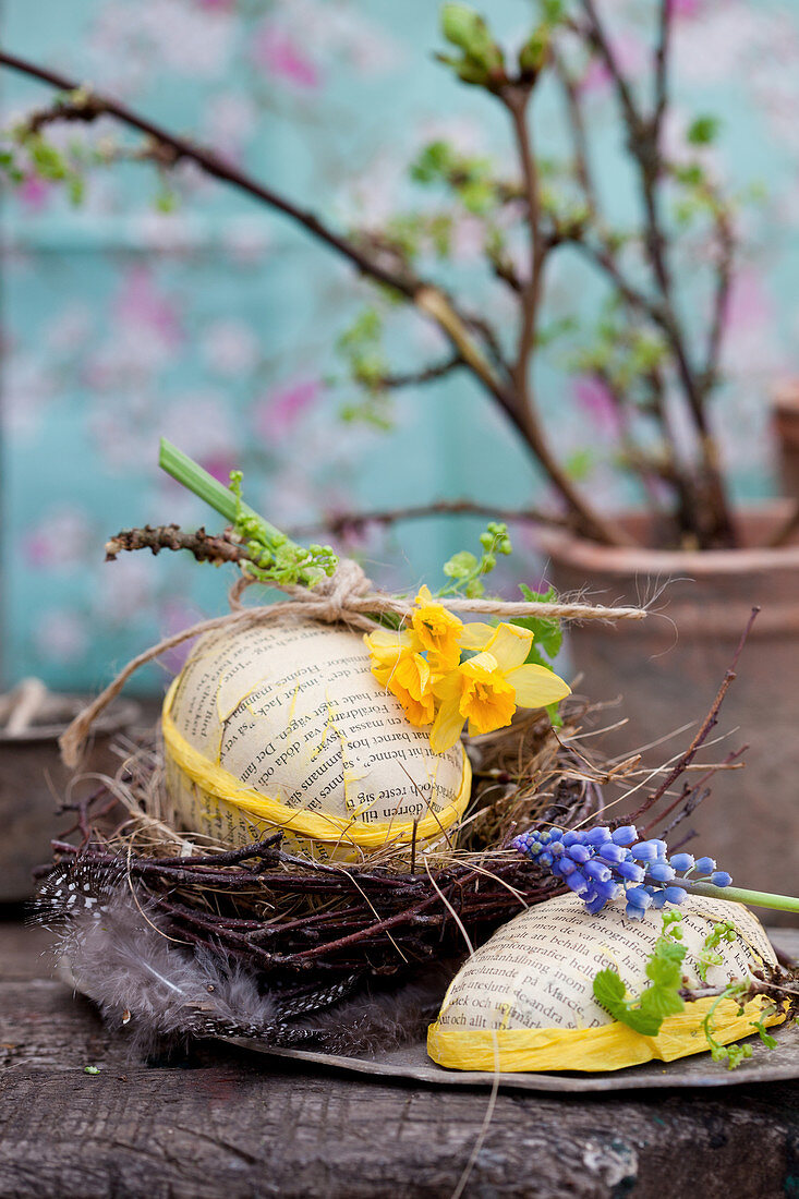 Selbstgemachtes Papp-Osterei in Nest aus Zweigen mit Blüten von Narzisse und Traubenhyazinthen