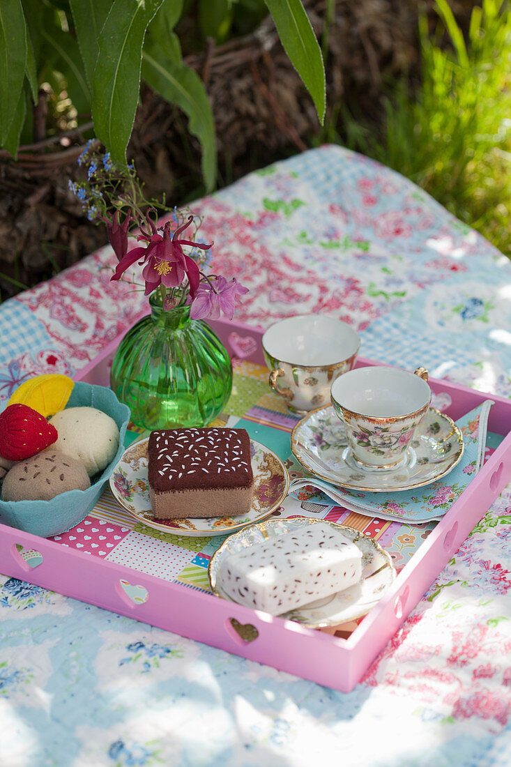 Handmade felt cakes and ice-cream and china teacups on tray on picnic blanket