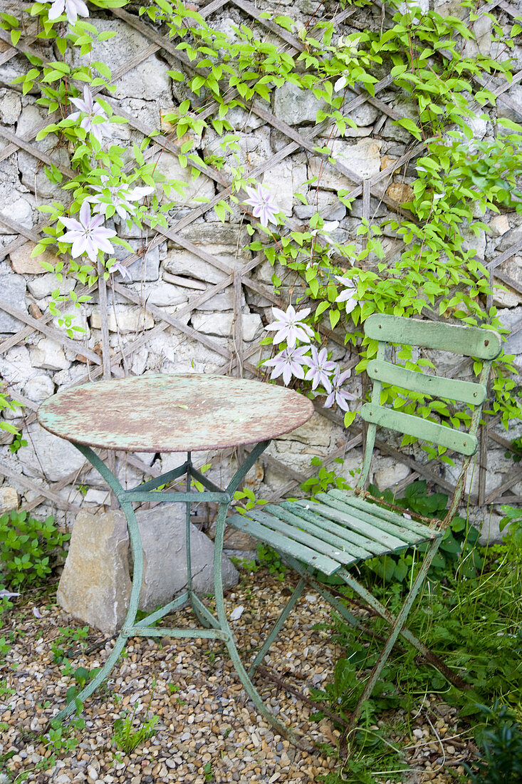 Rostige Gartenmöbel vor einer Natursteinmauer mit Clematis