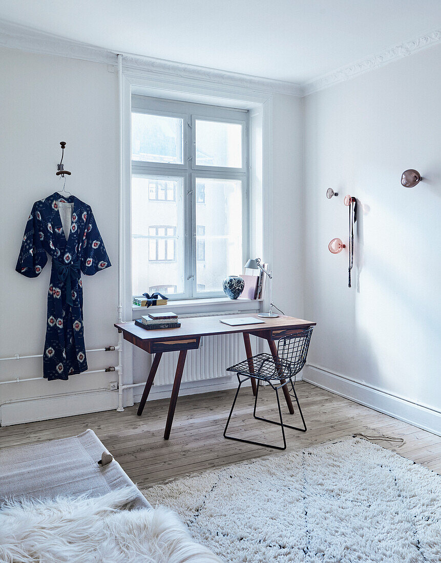 Klassikerstuhl und Schreibtisch vor Fenster, daneben Kimono an der Wand