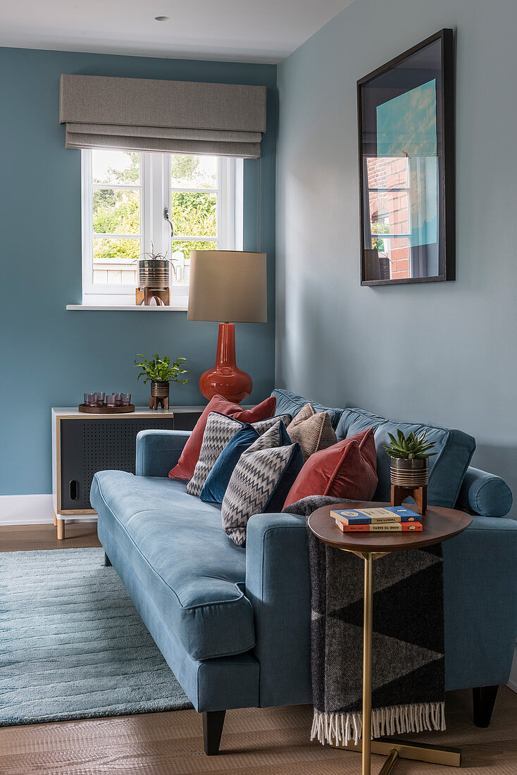 Rust-red scatter cushions on blue sofa against pale blue wall in living room