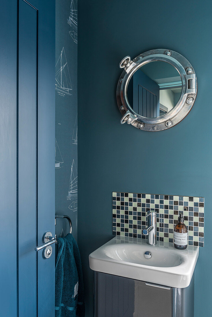 Mirror with porthole frame above sink in small blue bathroom