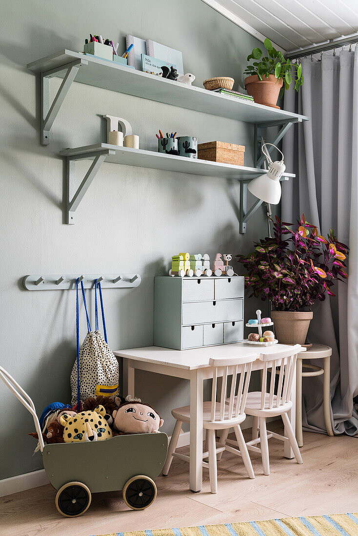 Table with chairs, doll's pram and shelves in nursery with green walls