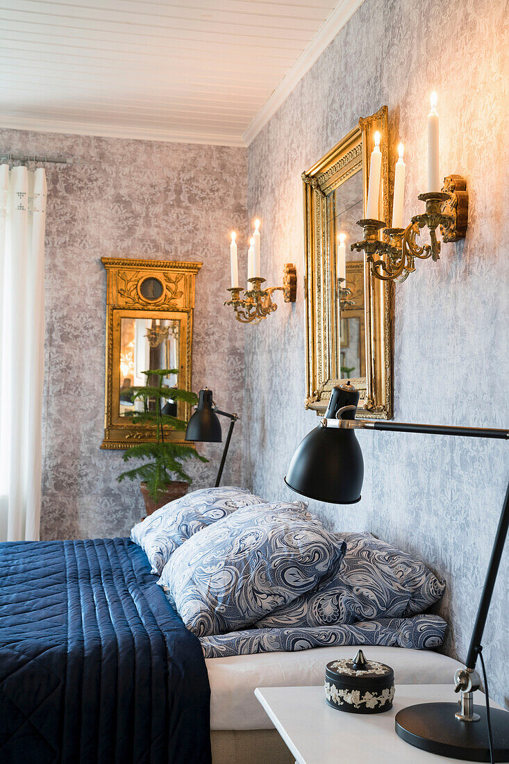 Doppelbett im Schlafzimmer mit gemustertem Tapete, Goldrahmenspiegel und brennenden Kerzen