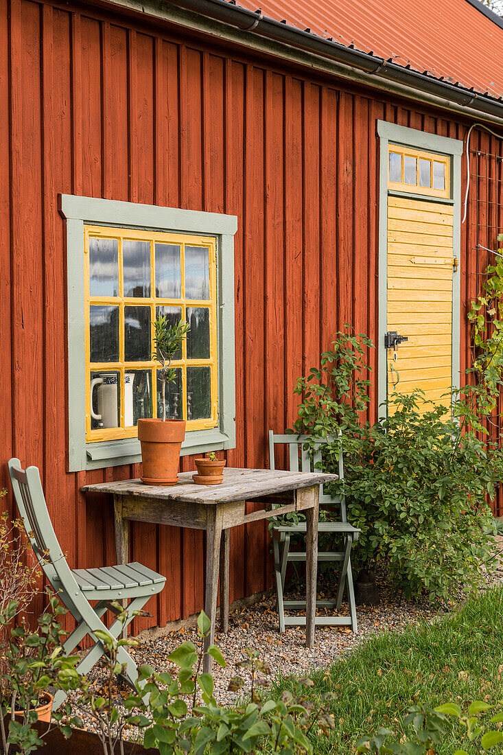 Sitzplatz mit altem Holztisch vorm Schwedenhaus mit gelbem Fenster