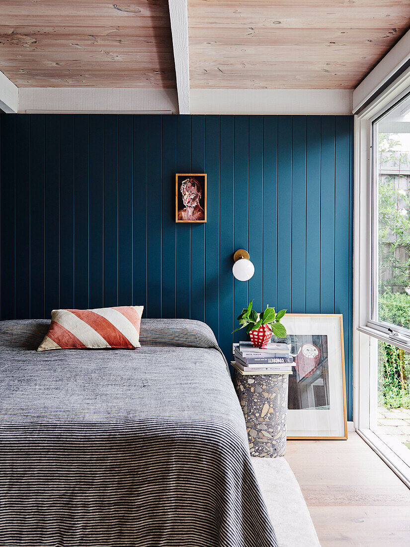 Double bed in front of petrol coloured wood panelling