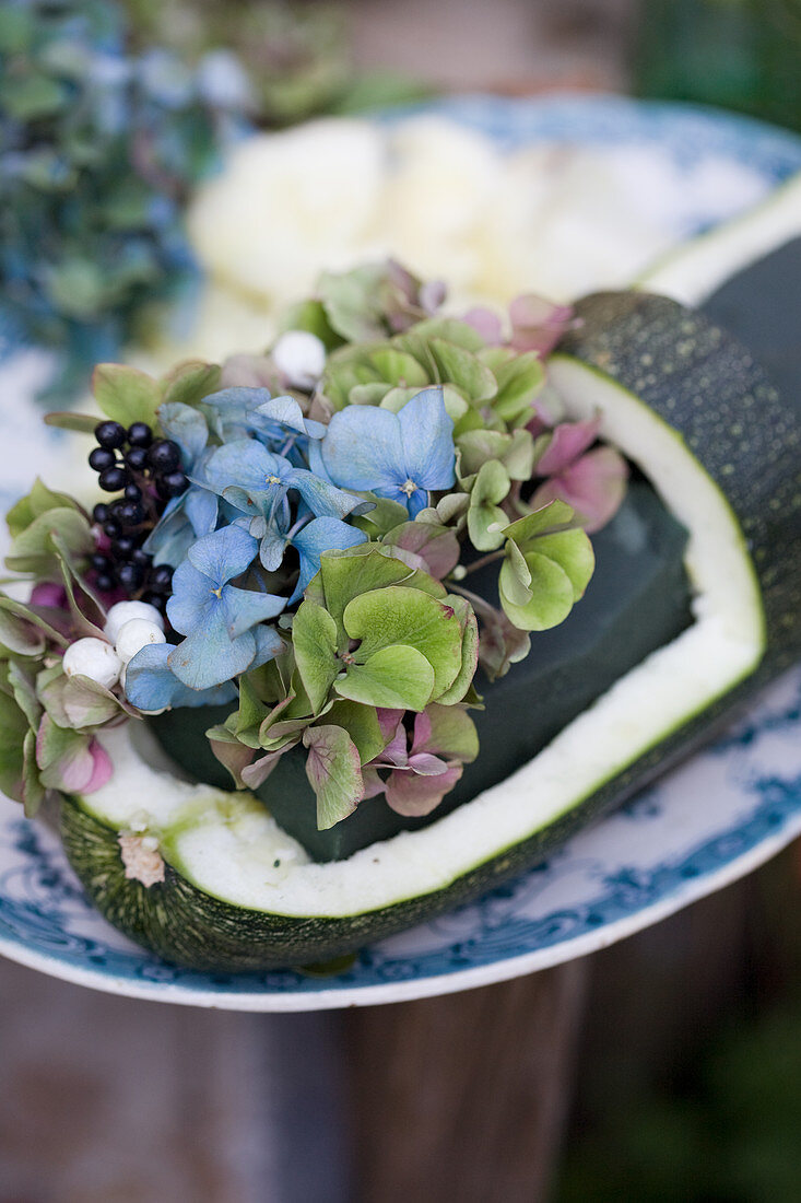 Arrangement of hydrangea blossoms, privet berries, and snowberry in hollowed out Zucchini