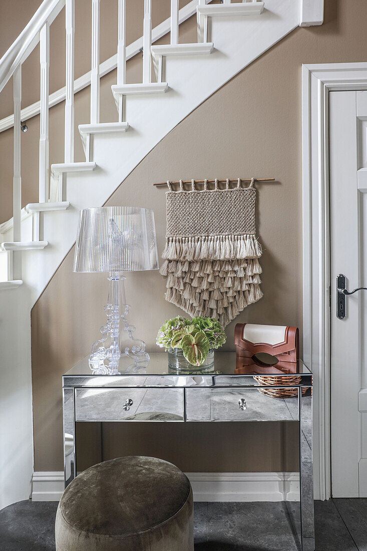 Mirrored table with drawers and designer lamp against staircase wall in hallway