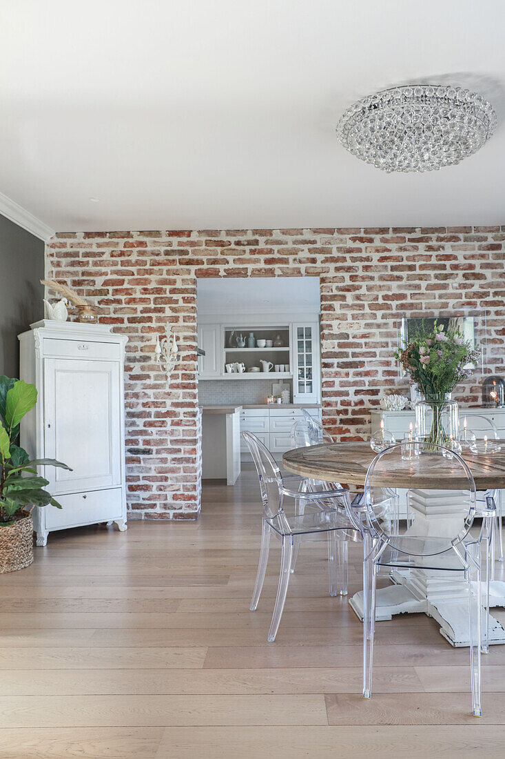 Round, solid-wood table and transparent chairs in front of brick wall
