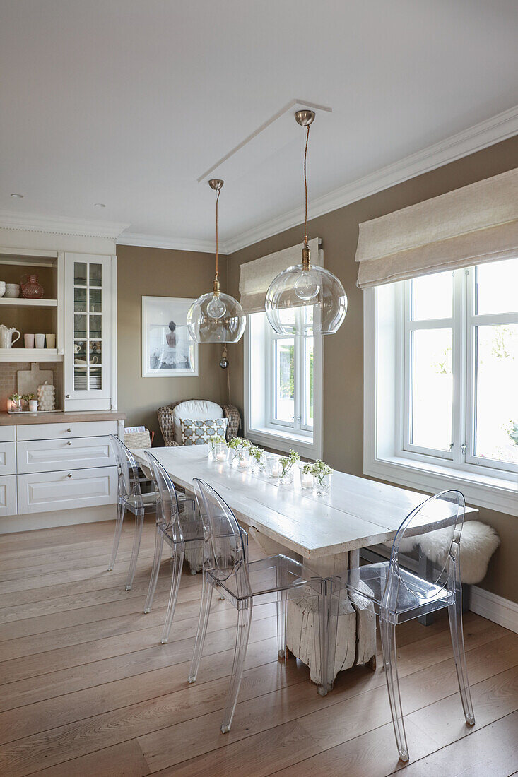 Long dining table and transparent chairs in kitchen with beige walls