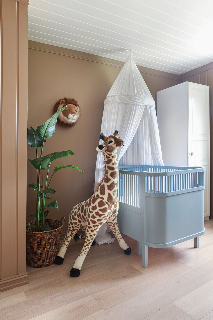 Houseplant and large plush giraffe next to cot with canopy