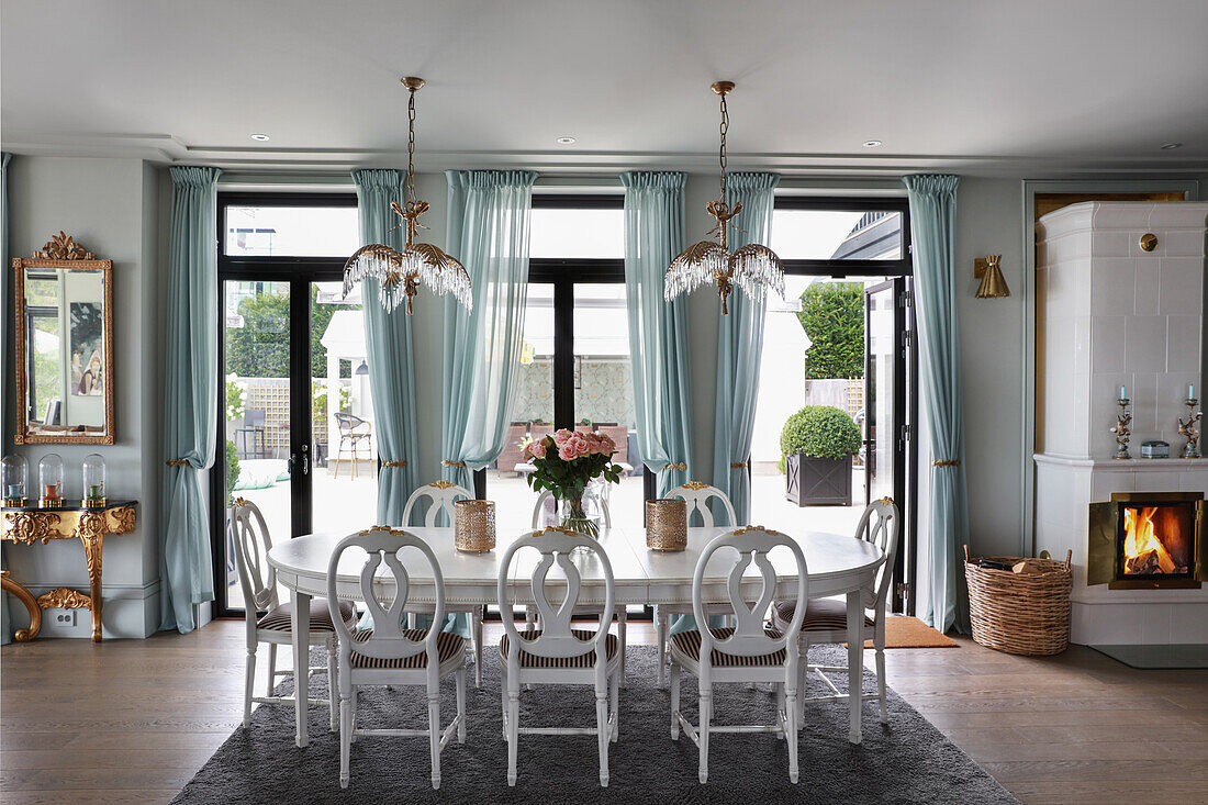 Weißer Esstisch mit Stühlen in offenem Wohnraum mit Fenstertüren und blauen Vorhängen