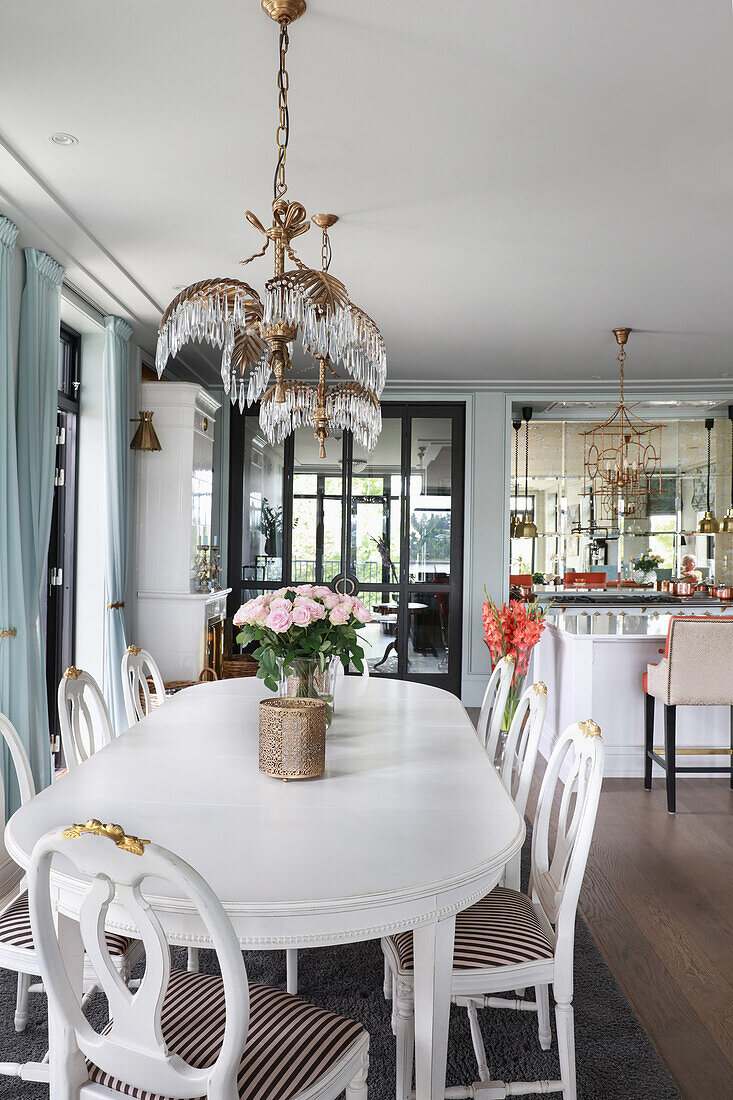 Weißer Esstisch mit Stühlen, darüber Designerleuchte in elegantem, offenem Wohnraum