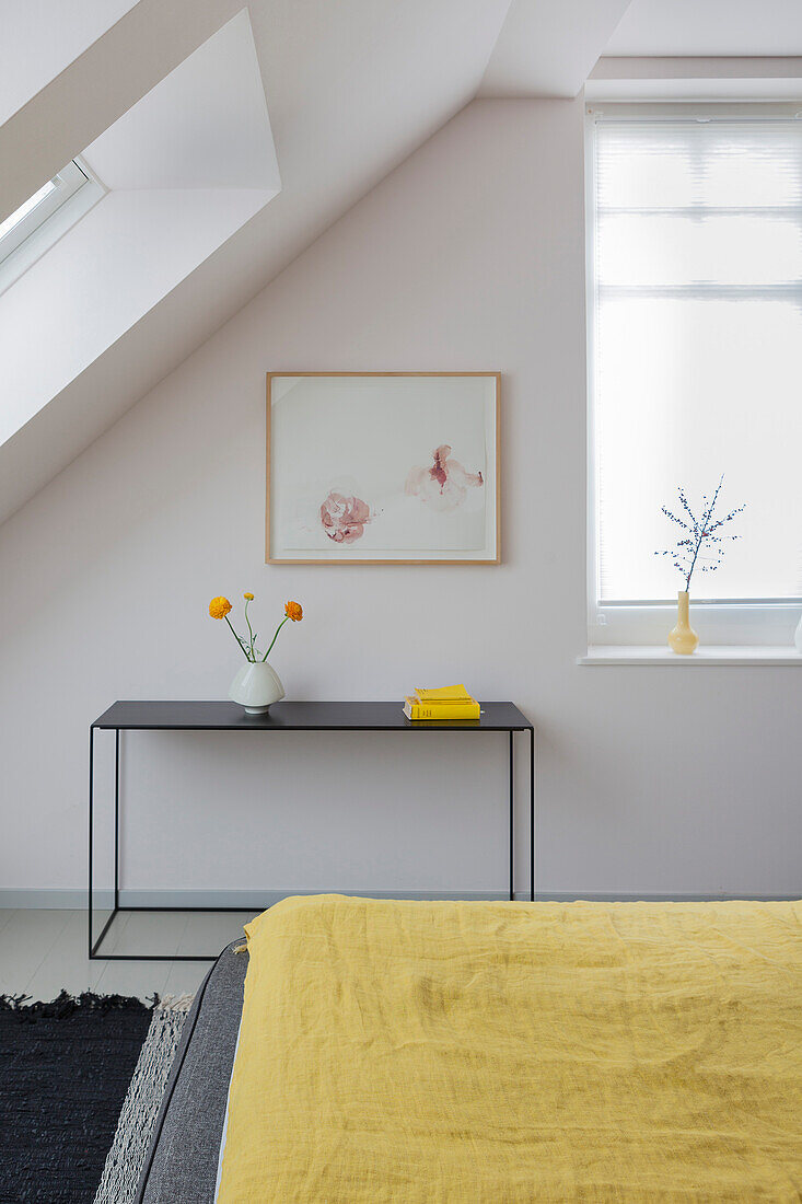 Blick über Bett mit gelber Tagesdecke auf Konsolentisch unter Dachschräge