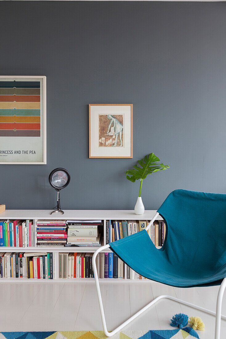 Blauer Sessel vor Bücherregal im Wohnzimmer mit dunkler Wand